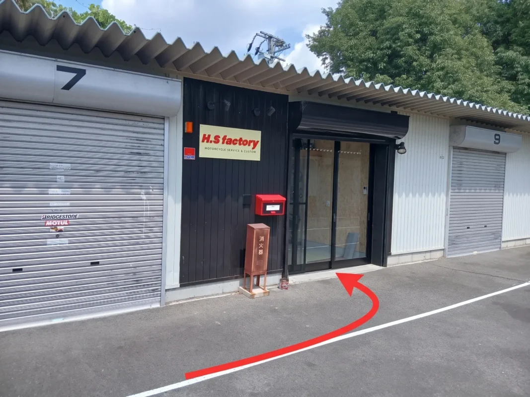 黒い外壁とH.S factory看板、赤いポストがある店舗入口の案内写真